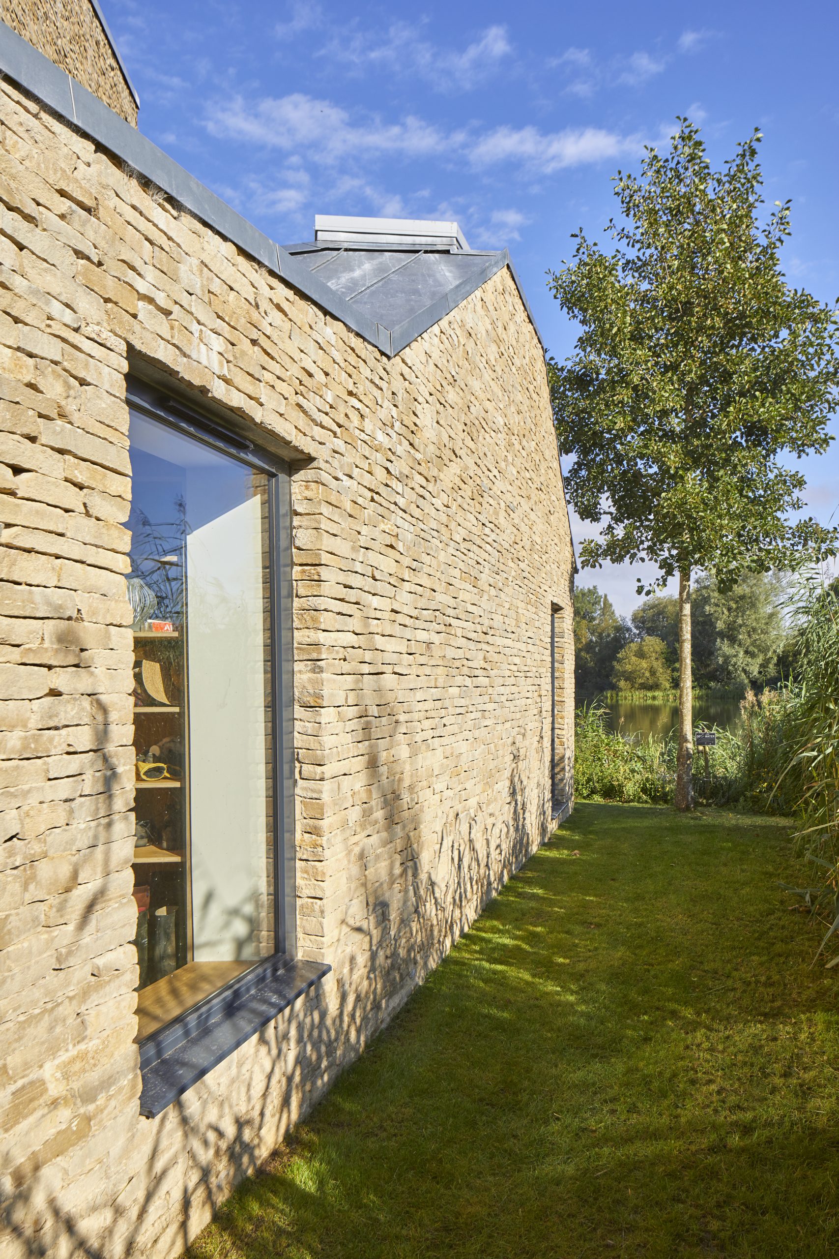 stone wall of modern house with lake side setting, large picture windows and a tree in the background