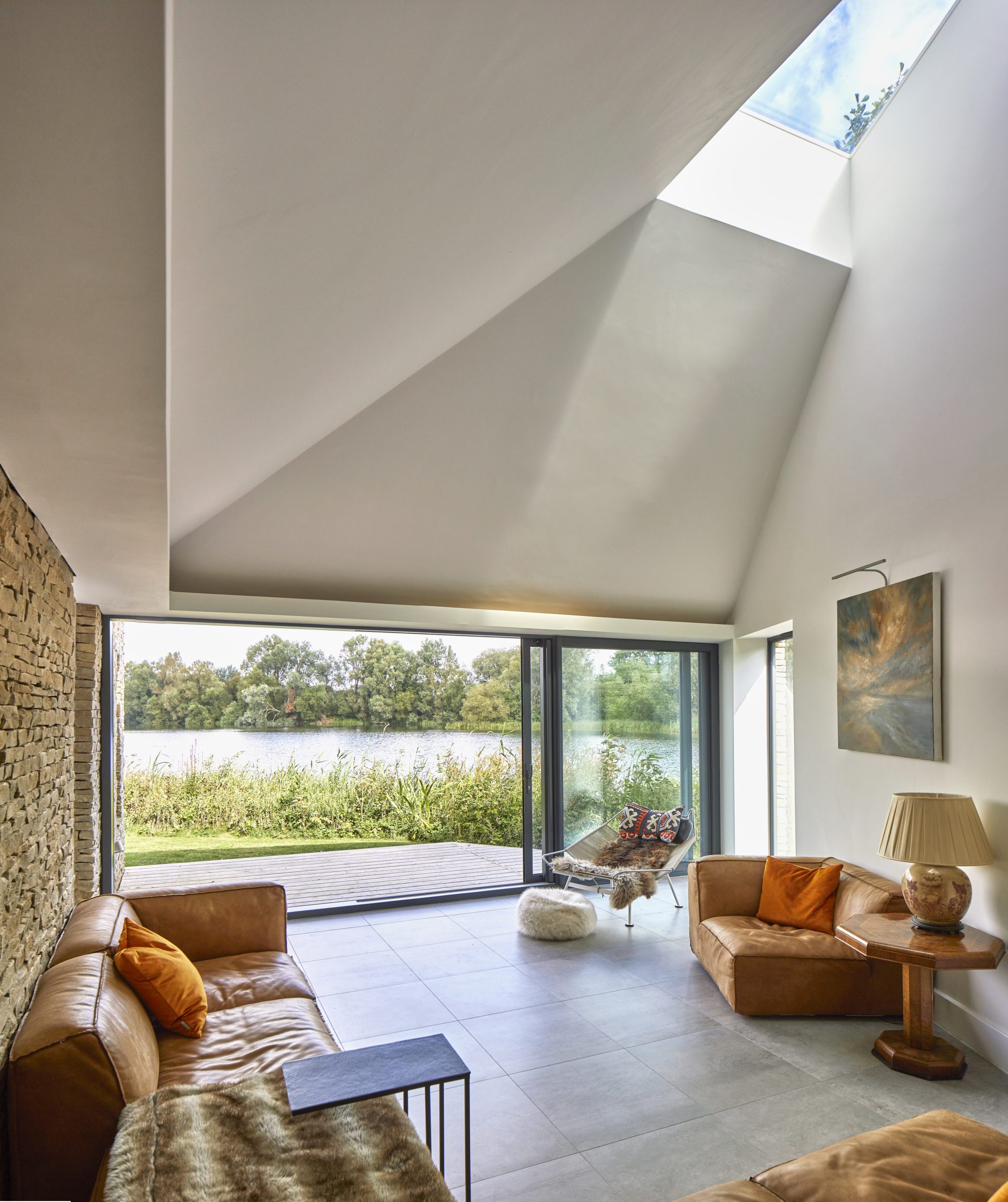 modern interior room with glazed roof light large sliding doors, modern stone floor with stone walls, modern art on the wall and brown leather seats