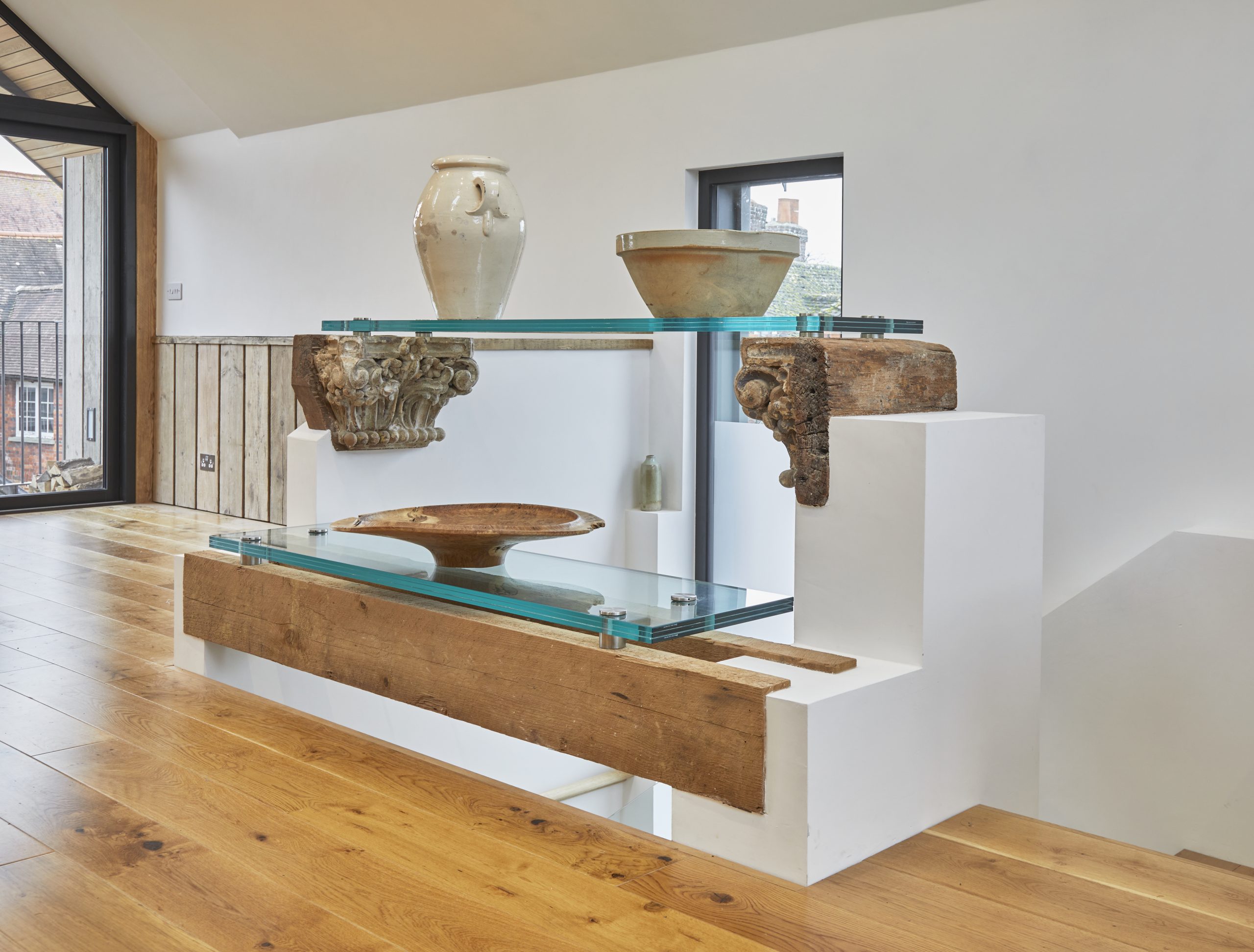 Open glass shelving with large oak beams over the staircase with pottery objects and wood carving
