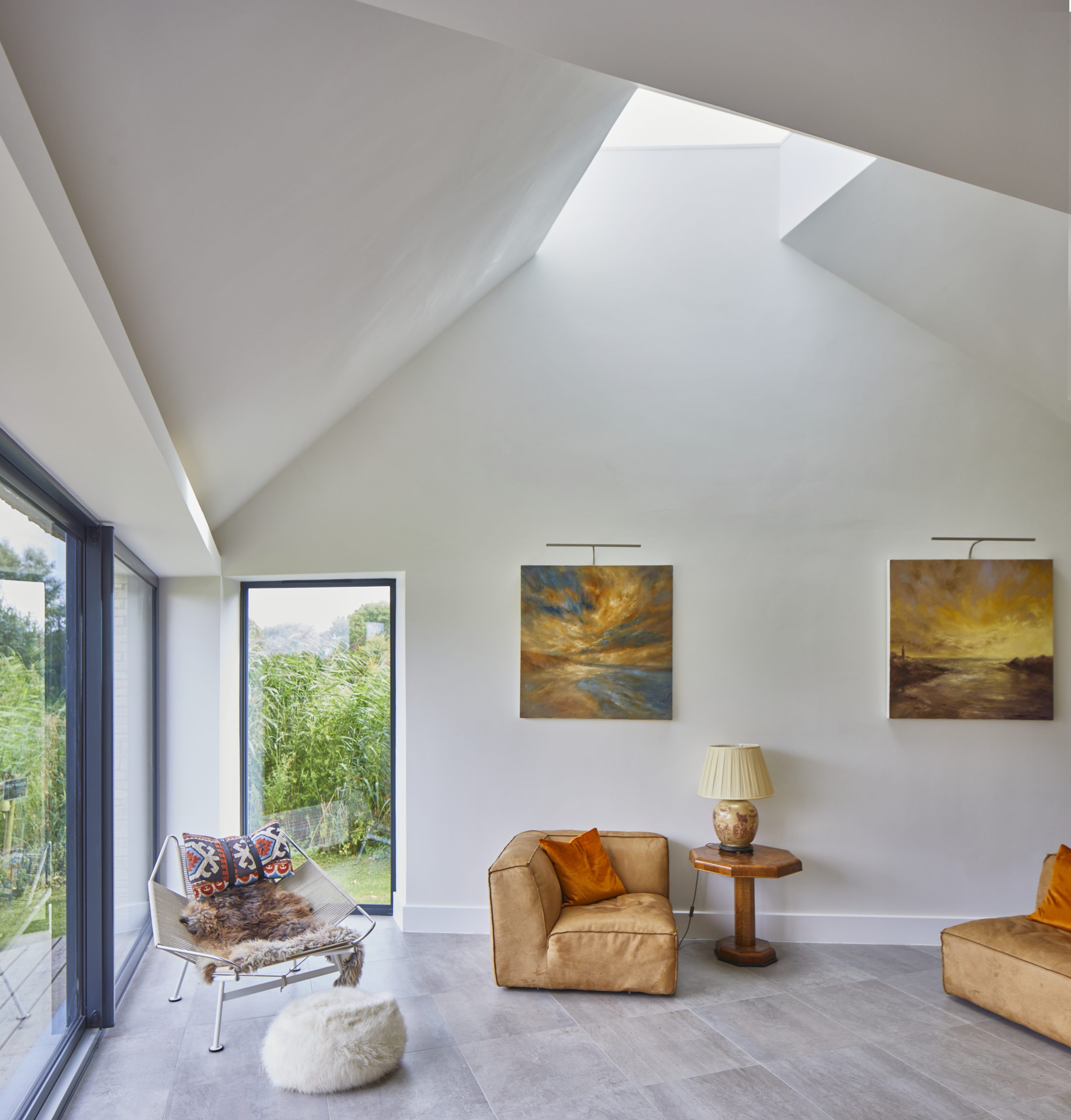 modern interior room with glazed roof light large sliding doors, modern stone floor with stone walls, modern art on the wall and brown leather seats