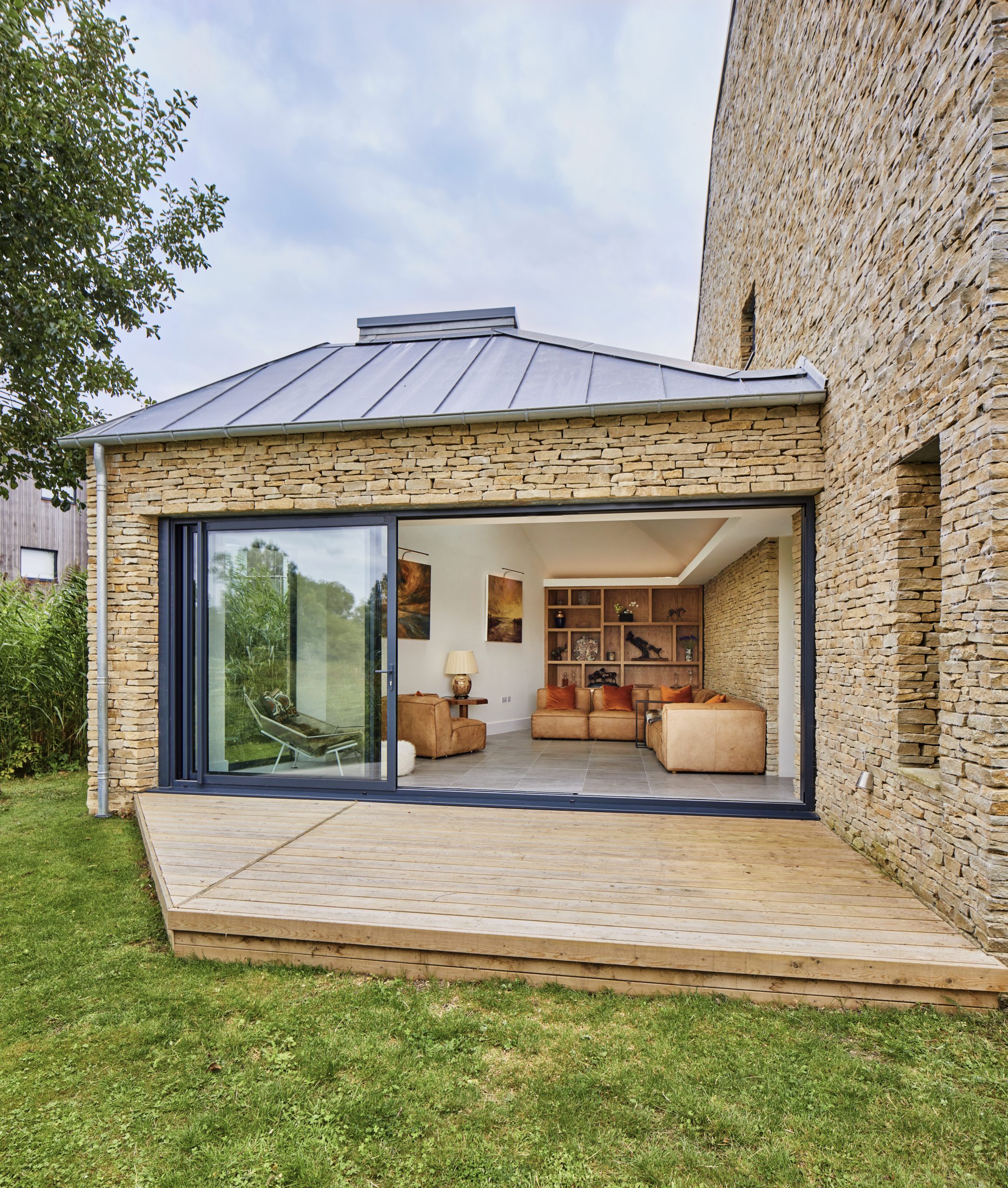 Modern stone face of lakeside house, with large sliding doors and picture windows